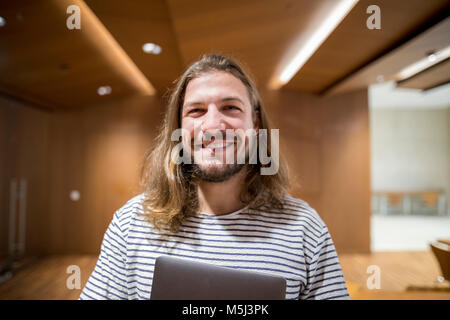 Portrait of laughing man with laptop in university Stock Photo