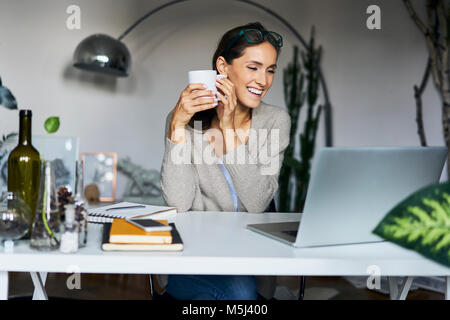 Happy young woman at home with laptop on desk Stock Photo