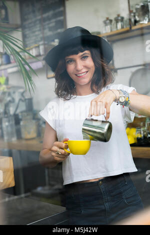 Portrait of woman with black hat behind the bar preparing a coffee Stock Photo