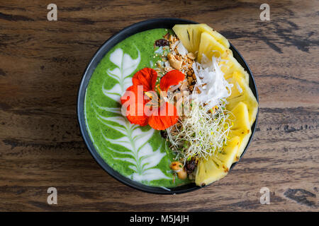 Decorated green smoothie bowl with pineapple and edible flower Stock Photo