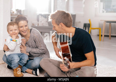Happy family sitting on the floor with father playing guitar Stock Photo