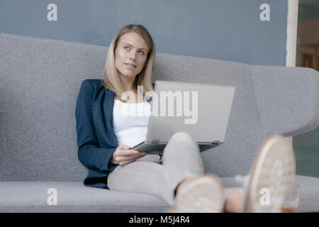 Portrait of pensive businesswoman sitting on couch with laptop Stock Photo