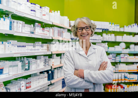 Portrait of smiling pharmacist at shelf with medicine in pharmacy Stock Photo