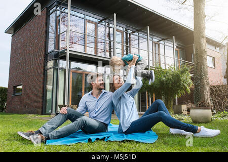 Happy parents with son sitting on blanket in garden in front of their home Stock Photo