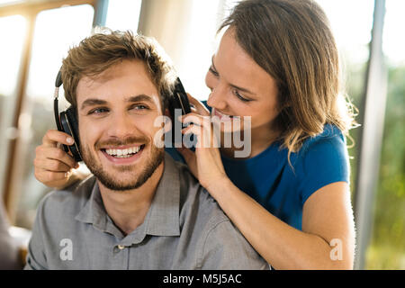 Smiling woman putting on headphones on boyfriend