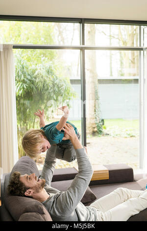 Happy father playing with son on sofa at home Stock Photo