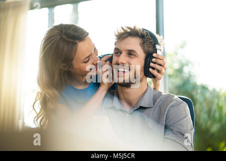 Smiling woman putting on headphones on boyfriend