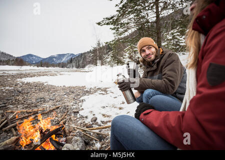 Couple on a trip in winter having a hot drink at camp fire Stock Photo