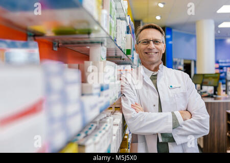Portrait of smiling pharmacist leaning against shelf with medicine in pharmacy Stock Photo