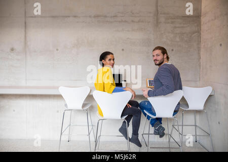 Young man and woman using moblie devices in concrete room Stock Photo