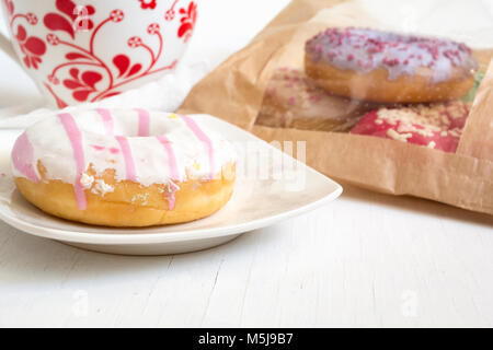 Donut on plate. Bag full of doughnuts and cup of tea. Stock Photo