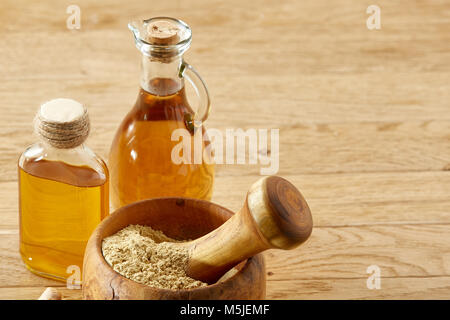 Beautiful kitchen still life two transparent glass oil jars, wooden mortar full of grind spicies and pestle with ginger root on rustic wooden table, s Stock Photo