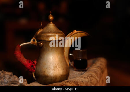 Old tea pot is standing on the edge of fireplace with a tea cup full of tea in the background, Aqaba, Jordan Stock Photo