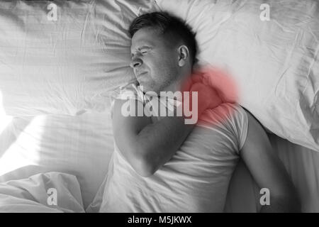 Caucasian young man having terrible pain in neck in bed in the morning Stock Photo