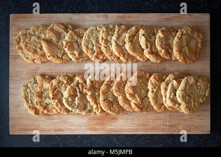 Two rows of freshly cooked plain American cookie biscuits laid out to cool on a wooden board. Stock Photo