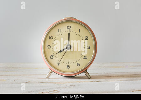 Retro alarm-clock with time of on white wooden table and pink pastel background. Close up. Stock Photo