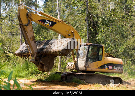 Cat 3200 trackhoe moving heavy timber crane mats along a gravel logging road in the Alabama River Swamp. Stock Photo