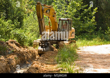 Cat 3200 trackhoe (track hoe, excavator, mechanical shovel) digging a drainage ditch along a gravel logging road in the Alabama River Swamp, in Clack  Stock Photo