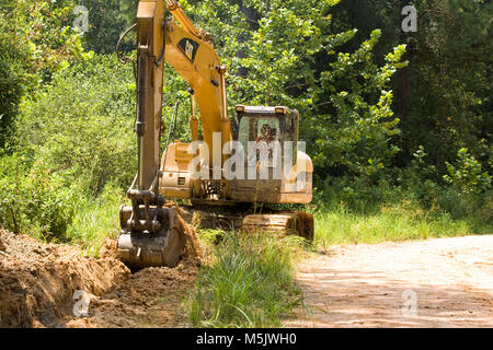 Cat 3200 trackhoe (track hoe, excavator, mechanical shovel) digging a drainage ditch along a gravel logging road in the Alabama River Swamp, in Clack  Stock Photo