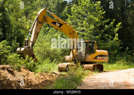 Cat 3200 trackhoe (track hoe, excavator, mechanical shovel) digging a drainage ditch along a gravel logging road in the Alabama River Swamp, in Clack  Stock Photo