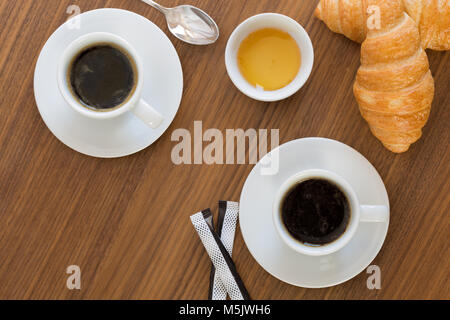 Two cups of coffee with croissants, honey and sachets sugar on  wooden table. top view Stock Photo
