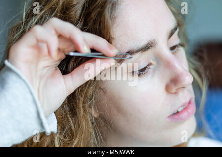 Photograph of a girl plucking her eyebrows with tweezers. Stock Photo