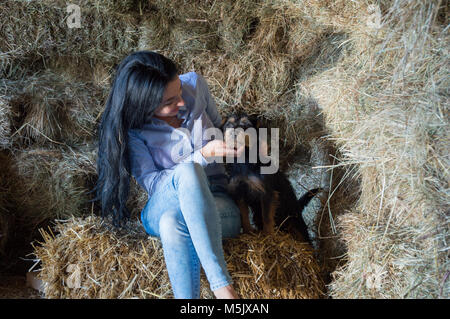 Black hair female in barn cuddling a little dog Stock Photo