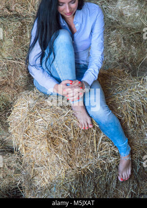 cropped image of female sitting on bales of hay smiling with hands leaned on one leg Stock Photo