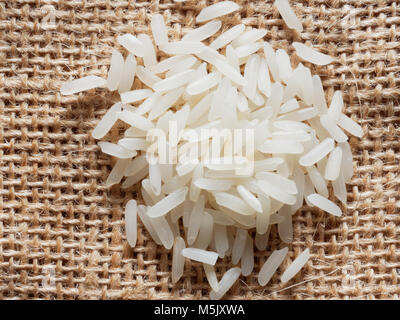 Pile of white raw rice over brown sackcloth background Stock Photo