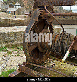 Old boat winch with rusty gear wheels and cogs, and steel cable, Charlestown Harbour slipway, Cornwall, England, UK Stock Photo