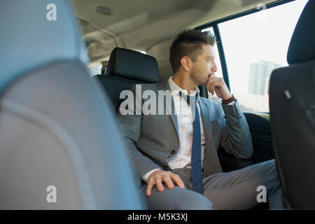 Young business man looking out the window sitting in car service limousine