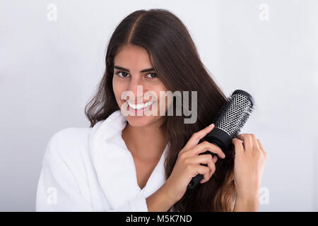 Portrait Of A Happy Woman In Bathrobe Combing Hair At Home Stock Photo