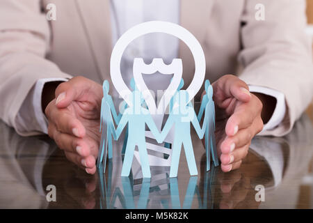 Woman's Hand Protecting Light Bulb Surrounded By Human Figures On Desk Stock Photo