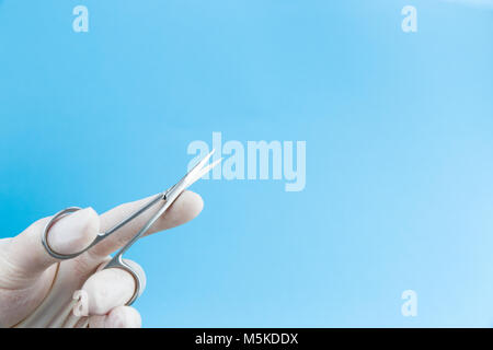 Scissors in doctors hands in white medical gloves isolated on blue background copy space. Studio Shot Stock Photo
