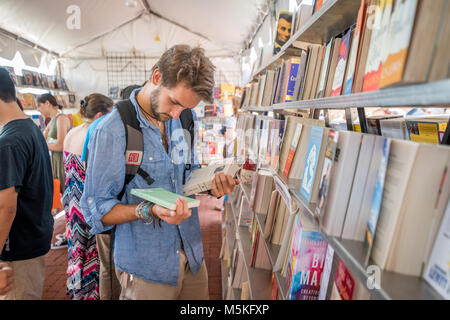 Young man reads the back of two books standing in front of bookshelf, Baltimore, Maryland. Stock Photo