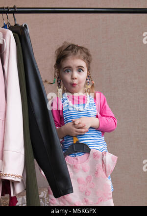 Little girl trying on a new dress. Small girl chooses dress. Little girl and clothes hangers shopping Stock Photo