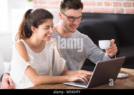 Smiling Young Couple Using Laptop On Table While Having Breakfast At Home Stock Photo