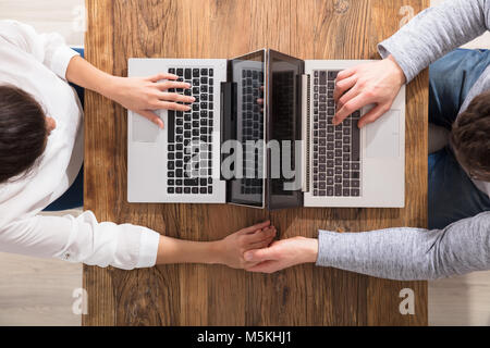 Overhead View Of Couple Sitting Face To Face Using Laptop On Table Stock Photo