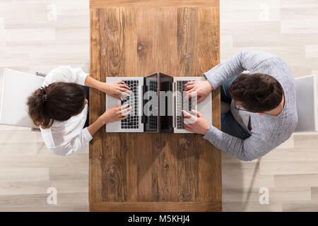 Overhead View Of Couple Sitting Face To Face Using Laptop On Table Stock Photo