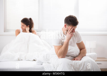 Worried Young Couple Sitting On Bed At Home Stock Photo