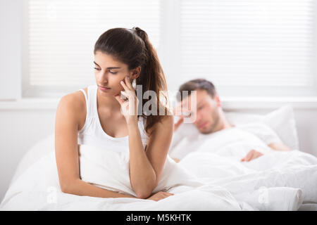 Young Woman Sitting On Bed Is Upset With Her Husband At Home Stock Photo