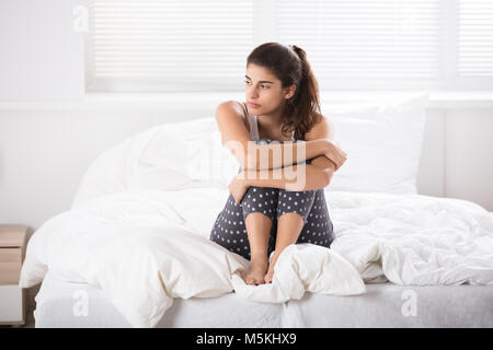 Contemplated Young Woman Sitting Alone On Crumpled Bed At Home Stock Photo