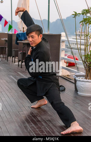 A Vietnamese man leads a group of tourists in a Tai Chi class at sunrise on the upper deck of a cruise ship in Halong Bay, Vietnam. Stock Photo