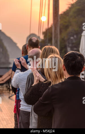 A Vietnamese man leads a group of tourists in a Tai Chi class at sunrise on the upper deck of a cruise ship in Halong Bay, Vietnam. Stock Photo
