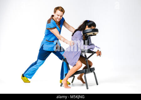 Theme massage and office. A young man with smiling therapist in blue suit is doing back and neck massage for young woman worker, business woman in a s Stock Photo