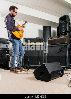 Photo of a man playing his electric guitar in a recording studio in front of amplifiers. Stock Photo