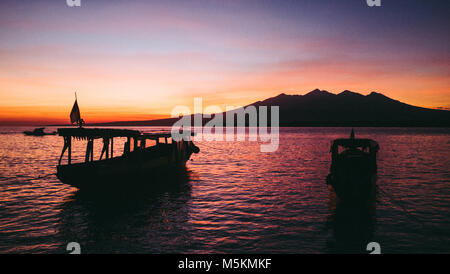 The sunrise above the volcano in Bali from the Gili Islands can be seen with two boats in the foreground Stock Photo