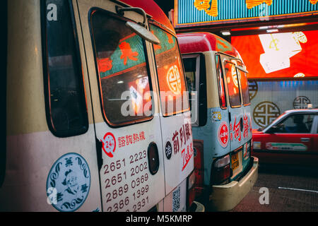 The reflection of the shops is seen in the back window of two minibuses in Hong Kong Stock Photo