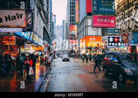 Shoppers walk through Ladies Market in the rain with the neon advertising billboards above Stock Photo