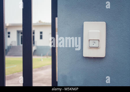Close up white doorbell or buzzer button on concrete wall beside doorway with house in the background. Stock Photo